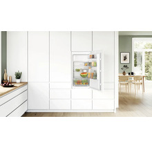 Einbaukühlschrank in moderner weißer Küche mit geöffneter Tür und gefüllten Fächern und Ablagen.