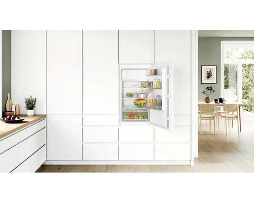 Einbaukühlschrank in moderner weißer Küche mit geöffneter Tür und gefüllten Fächern und Ablagen.