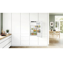 Einbaukühlschrank integriert in eine moderne weiße Küchenzeile mit offener Kühlschranktür und gefüllten Glasablagen und Gemüseschublade.