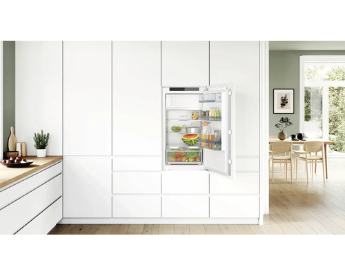 Einbaukühlschrank integriert in eine moderne weiße Küchenzeile mit offener Kühlschranktür und gefüllten Glasablagen und Gemüseschublade.