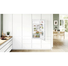 Einbaukühlschrank in einer modernen weissen Einbauküche mit offener Tür und gefüllten Ablagefächern.