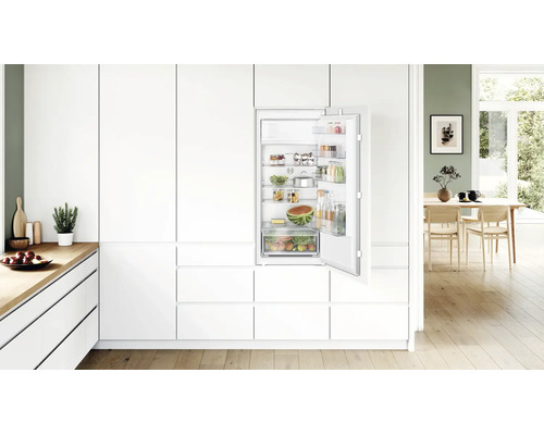 Einbaukühlschrank in einer modernen weissen Einbauküche mit offener Tür und gefüllten Ablagefächern.