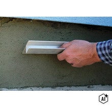Eine Hand hält ein Sockelprofil an eine frisch verputzte Wand zur Montage. (Image AI modified or generated)