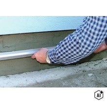 Eine Abziehlatte wird verwendet, um frischen Sockelputz an einer Hauswand glattzustreichen. (Image AI modified or generated)