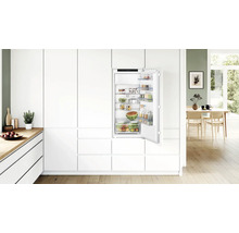 Einbaukühlschrank in einer modernen weißen Küche mit offener Tür, gefüllt mit Lebensmitteln, Bosch Logo sichtbar im Innenraum.