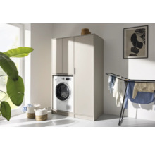 Moderner Waschmaschinenschrank und Hochschrank in Beige in einem hellen, aufgeräumten Hausarbeitsraum mit Wäscheständer und Pflanze.
