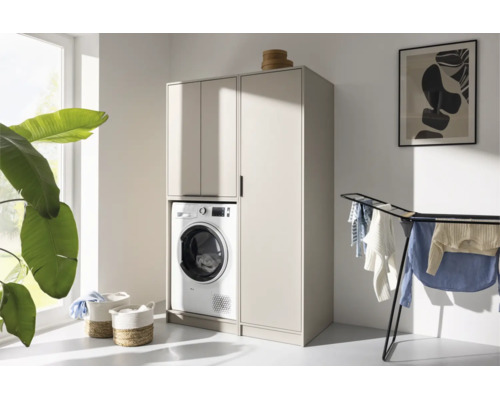 Moderner Waschmaschinenschrank und Hochschrank in Beige in einem hellen, aufgeräumten Hausarbeitsraum mit Wäscheständer und Pflanze.