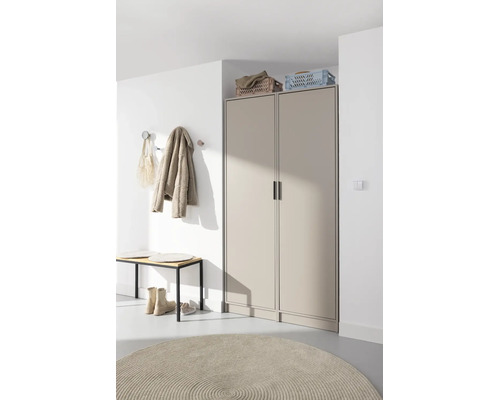 Modernes Entree mit beigem zweitürigen Garderobenschrank, Holzbank, Kleiderhaken an weißer Wand und rundem Teppich.