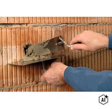 Eine Person trägt mit einer Maurerkelle und einem Mörtelbrett Mörtel auf eine Ziegelwand auf. (Image AI modified or generated)