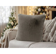 Weiches, graues Kunstfell-Kissen auf einem Sofa in weihnachtlicher Atmosphäre mit einem geschmückten Tannenbaum im Hintergrund.