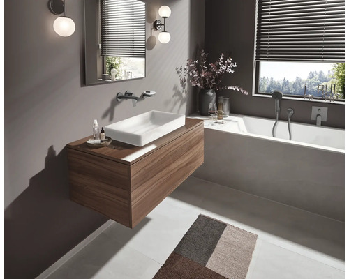 Modernes Badezimmer mit Waschtisch in Holzoptik, weißem Aufsatzwaschbecken, integrierter Badewanne, Wandarmaturen und stimmungsvoller Beleuchtung.