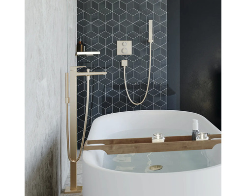 Modernes Badezimmer mit freistehender Badewanne, bodenstehender Wannenarmatur und Unterputz Armatur mit Handbrause vor geometrischen Wandfliesen.