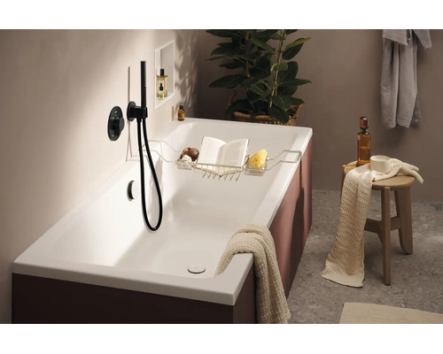 Moderne Badewanne mit Wannenablage, Buch, Schwamm und Duscharmatur. Ein stilvolles Badezimmerambiente mit Handtuch und Ablagehocker.