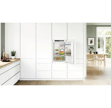 Einbaukühlschrank in moderner, weißer Küche mit geöffneter Tür und gefüllten Ablagefächern.