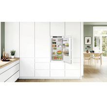 Einbaukühlschrank in moderner, weißer Einbauküche mit offener Tür und gefüllten Regalfächern und Gemüsefach.