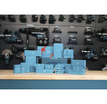 Makita Werkzeug Adventskalender mit vierundzwanzig nummerierten Geschenkschachteln auf einer Werkbank vor einer Werkzeugwand.