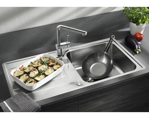 Moderne Edelstahl Küchenspüle mit integrierter Armatur, Abtropffläche und einer Auflaufform sowie einer Pfanne in einer funktionalen Küche.