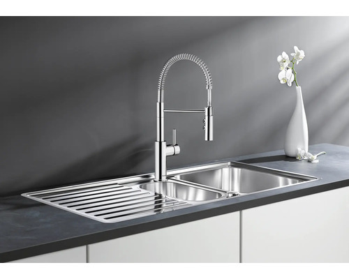 Moderne Edelstahl Küchenspüle mit Abtropffläche und professioneller Küchenarmatur mit Schlauchbrause auf einer dunklen Arbeitsplatte.