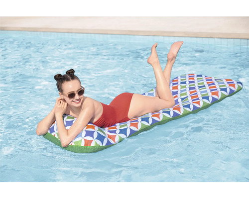 Eine junge Frau entspannt auf einer aufblasbaren Poolliege mit buntem geometrischem Muster auf dem Wasser eines Swimmingpools.