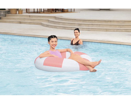 Ein junges Mädchen entspannt in einem runden aufblasbaren Schwimmreifen in einem Swimmingpool, im Hintergrund ist eine weitere Person zu sehen.