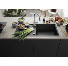 Moderne schwarze Einbauspüle mit Abtropffläche und Edelstahlarmatur in einer organisierten Küche mit frischen Zutaten auf der Arbeitsplatte.