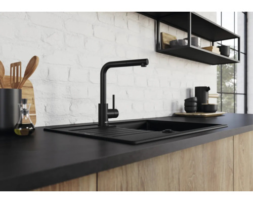 Moderne schwarze Küchenarmatur mit Spülbecken vor einer weißen Ziegelwand in einer Küche mit Holzfronten.
