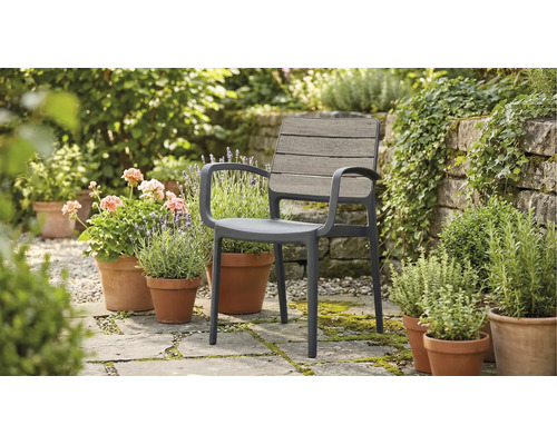 Gartenstuhl mit Armlehnen auf einer Steinterrasse umgeben von Blumentöpfen im Garten.
