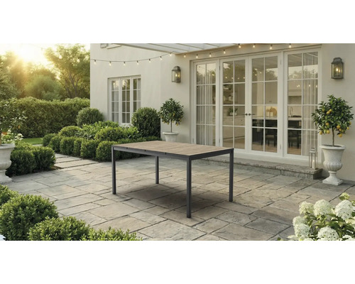 Gartentisch mit Holzoberfläche und Metallgestell auf einer gepflasterten Terrasse vor einem Wohnhaus mit großen Fenstertüren.