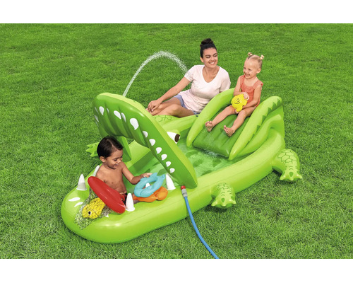 Aufblasbarer Krokodil Planschbecken Spielcenter mit Rutsche und integriertem Sprüher für Kinder auf einer Rasenfläche mit einer Frau und zwei Kindern.