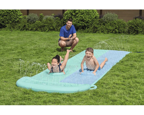 Zwei Kinder gleiten auf einer aufblasbaren Wasserrutsche im Garten, während ein Erwachsener zuschaut.