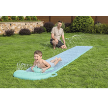 Ein Kind rutscht auf einer Wasserrutsche mit Sprühfunktion über eine Rasenfläche im Garten, während ein Mann im Hintergrund zuschaut.