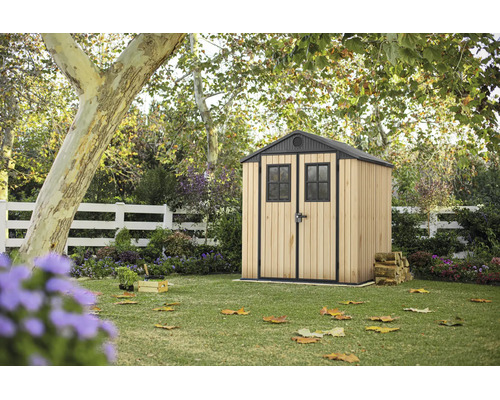 Gerätehaus aus Holz und Metall in einem Garten mit Rasenfläche unter Bäumen.
