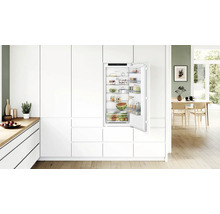Einbaukühlschrank in moderner, weißer Einbauküche mit offener Tür, gefüllt mit frischen Lebensmitteln und Bosch Logo.