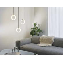 Drei moderne, ringförmige Pendelleuchten hängen über einem grauen Sofa mit Fellauflage in einem hellen, stilvoll eingerichteten Wohnzimmer.