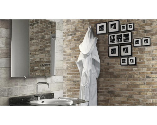 Badezimmer mit Ziegelsteinoptik Wandfliesen, Spiegel, Waschbecken und einem Bademantel an der Wand