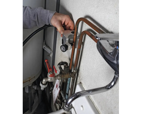 Hand legt Thermometer an Kupferrohr einer Wasserinstallation mit Mischbatterie und Absperrventil