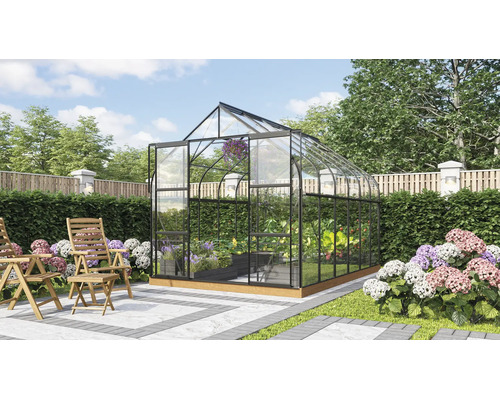 Freistehendes Gewächshaus mit Glaswänden und Metallrahmen in einem gepflegten Garten mit Holzstühlen auf einer Terrasse.