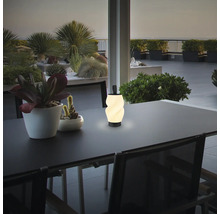 Eine moderne LED Tischleuchte mit gewundenem Lampenschirm steht abends auf einem Esstisch auf einer Terrasse.