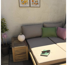 Gemütliche Loungeecke im Freien mit Holzsofa, Beistelltisch, Deko-Kissen, einer kleinen Lampe und Zitrusbildern an der strukturierten Wand.