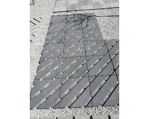 Gehweg aus diagonal verlegten Betonpflastersteinen mit Fugen auf einer Kiesfläche im Außenbereich