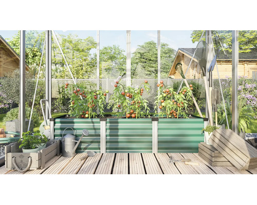 Ein Hochbeet aus profiliertem Metall in einem Gewächshaus mit Tomatenpflanzen, Gartenwerkzeugen und Holzkisten auf einem Holzterrassenboden.