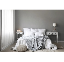 Modern eingerichtetes Schlafzimmer mit Doppelbett, weißen Textilien, zwei Nachttischen und dekorativem Sitzhocker auf hellem Bodenbelag.