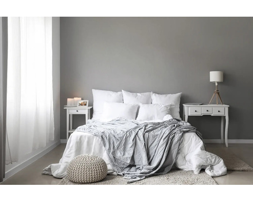 Modern eingerichtetes Schlafzimmer mit Doppelbett, weißen Textilien, zwei Nachttischen und dekorativem Sitzhocker auf hellem Bodenbelag.