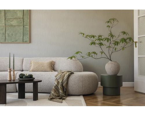 Modernes Wohnzimmer mit strukturierter Tapete, geschwungenem Sofa, dunklem Couchtisch, Beistelltisch und Zimmerpflanze in Vase.