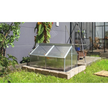 Ein Frühbeet mit Aluminiumrahmen und Hohlkammerplatten in einem Garten auf einer gemauerten Umrandung vor einer Hauswand.