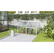 Ein kleines Frühbeet aus Aluminium und Hohlkammerplatten im Garten neben einer Gießkanne mit zwei aufklappbaren Dachfenstern für den Anbau.