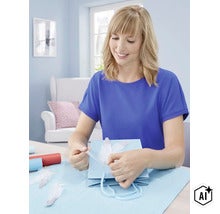 Eine Frau beim Verpacken eines Geschenks mit einer Geschenktüte und dekorativen Federn in einem hell eingerichteten Raum. (Image AI modified or generated)