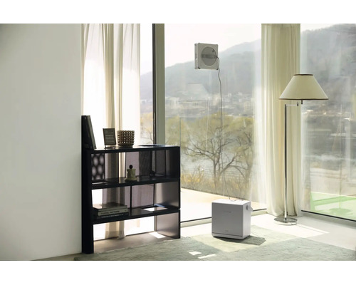 Ein automatischer Fensterputzroboter reinigt eine große Glasfront in einem hellen, modern eingerichteten Wohnraum.
