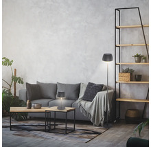 Modernes Wohnzimmer mit einer Tischleuchte und einer Stehleuchte mit gefaltetem Lampenschirm auf einem grauen Sofa vor einer Wand mit Struktur.