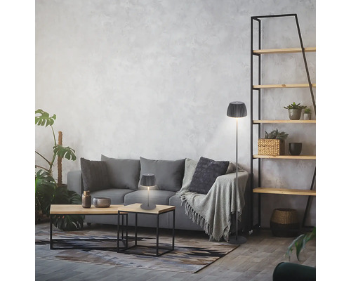 Modernes Wohnzimmer mit einer Tischleuchte und einer Stehleuchte mit gefaltetem Lampenschirm auf einem grauen Sofa vor einer Wand mit Struktur.